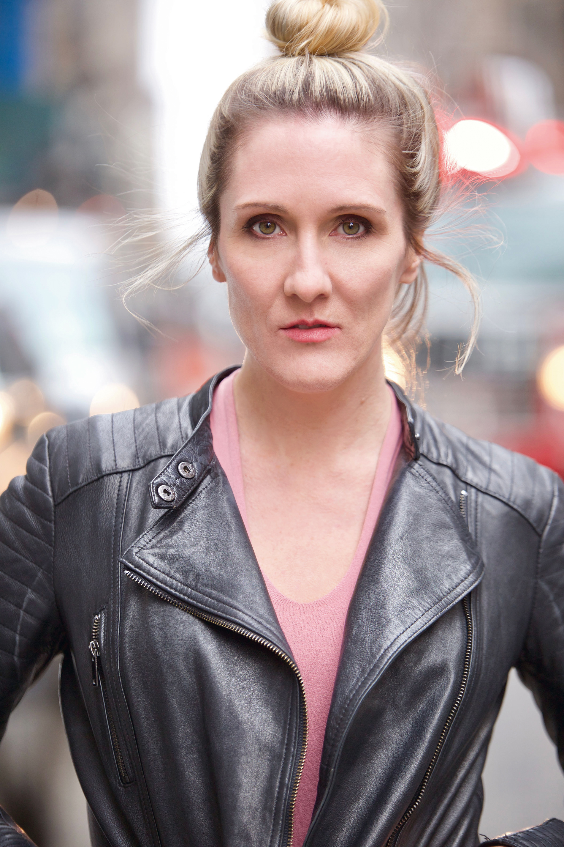 A woman in black leather jacket standing on sidewalk.