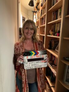 A woman holding a clapperboard in front of some bookcases.